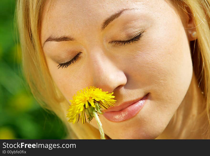 The beautiful girl enjoys aroma of a yellow flower. The beautiful girl enjoys aroma of a yellow flower