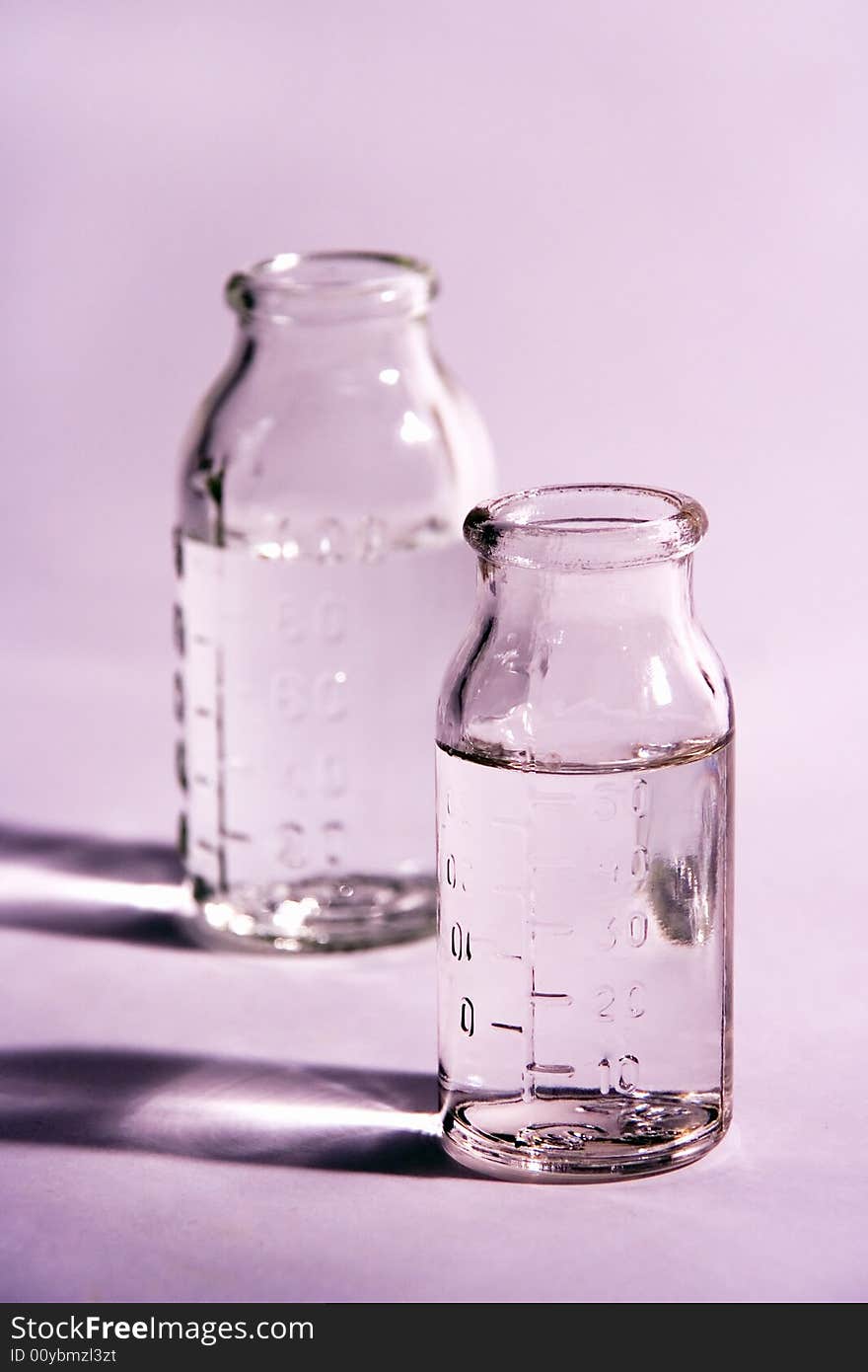 Two glass  measure bottles on violet background. Two glass  measure bottles on violet background