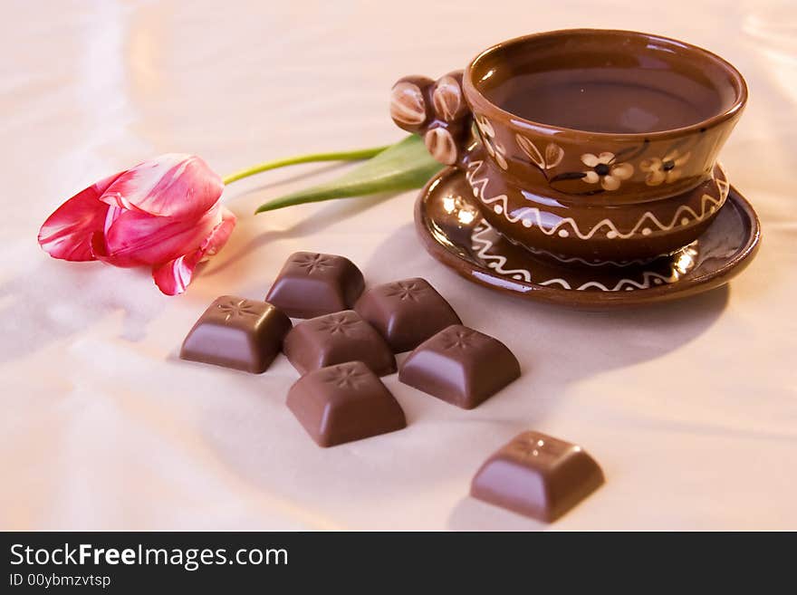 A photo of a cup of tea and a red tulip. A photo of a cup of tea and a red tulip