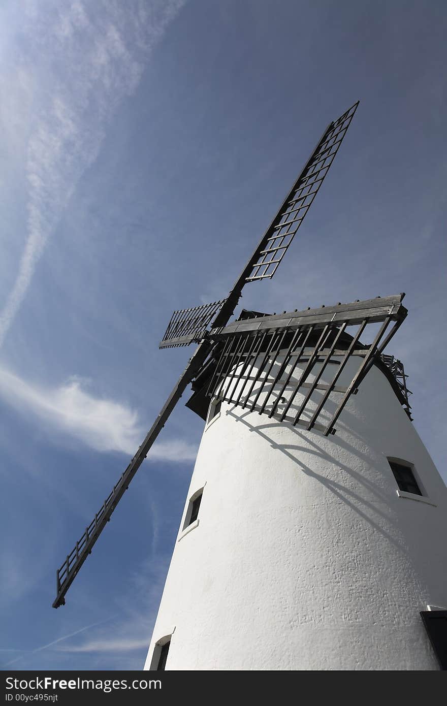 White windmill with black sails against blue sky
