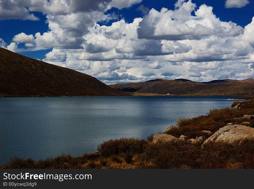 When travelling in Tibet of China, a  beautiful lake on field appears in front of us, with a lot of clouds in the sky.