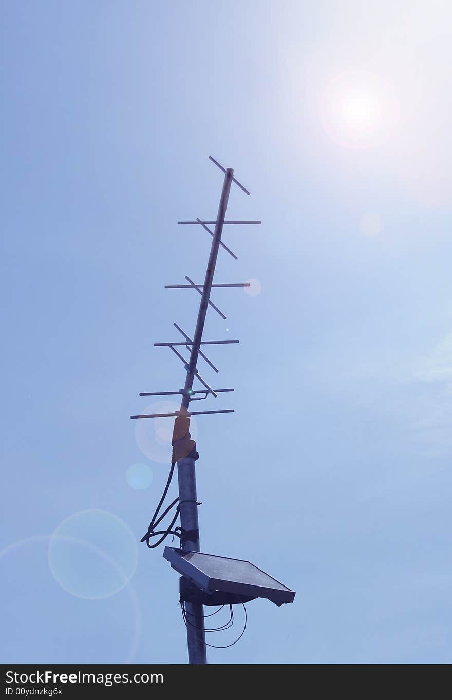 An antenna with solar power device on blue sky background with a sun glare. An antenna with solar power device on blue sky background with a sun glare