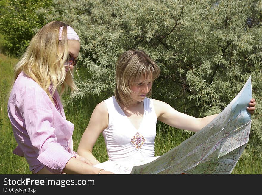 Two beautiful girls look at the map on nature