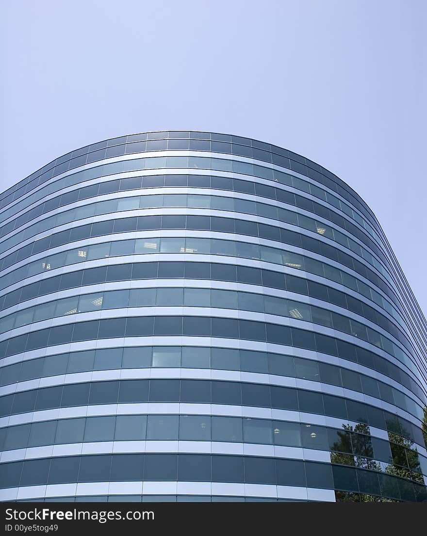 A modern curved blue glass building against a blue sky. A modern curved blue glass building against a blue sky