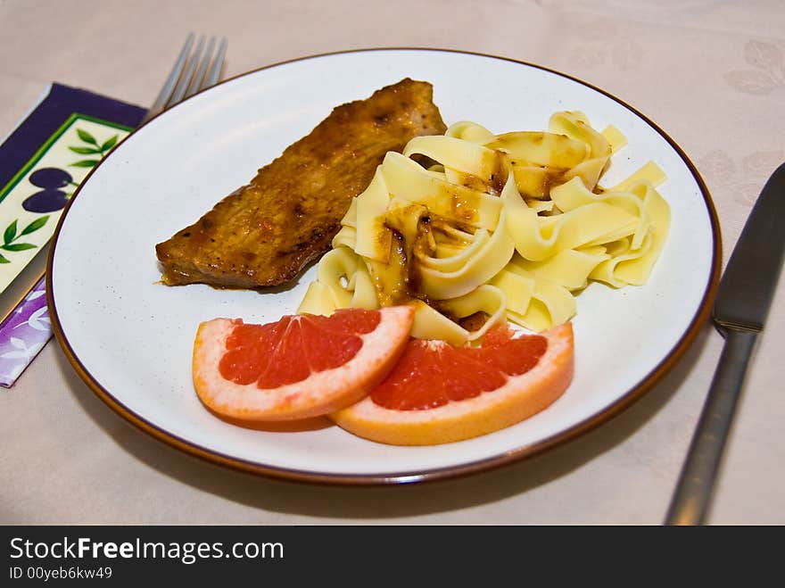 A closeup of a plate of Italian veal cutlet with pasta and graperuit. This dish is called Scaloppine al Pompelmo.