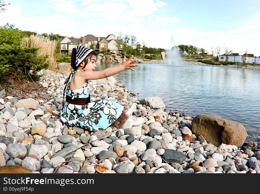 Two year old girl dressed up by the lake throwing rocks