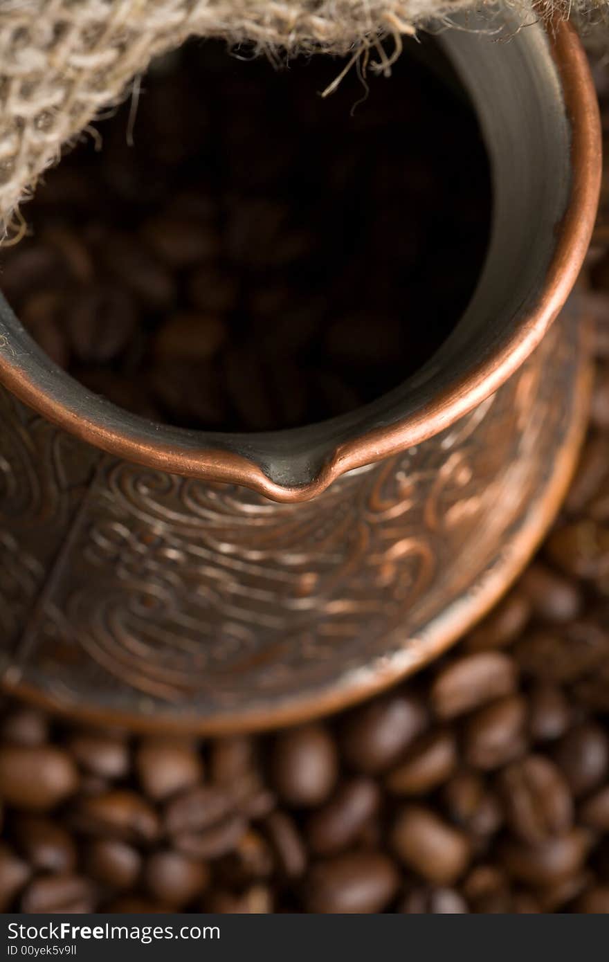 Cezve with freshly roasted coffee beans on sackcloth. Shallow depth of field. Focus on cezve throat