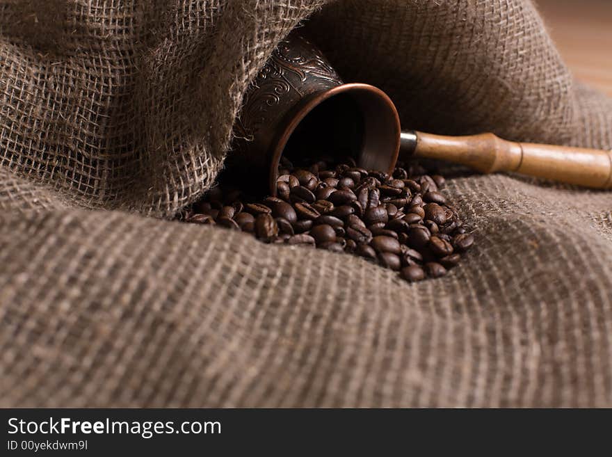 Cezve with freshly roasted coffee beans on sackcloth. Shallow depth of field. Focus on center of image