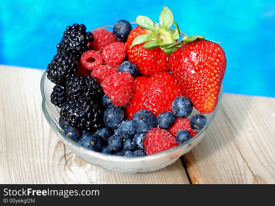 Bowl of mixed berries on a wooden deck near a pool. Bowl of mixed berries on a wooden deck near a pool