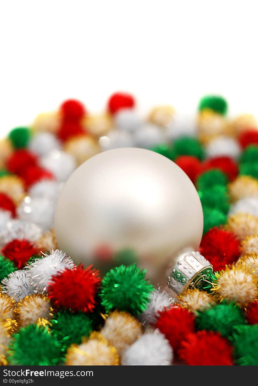 Silver Christmas bauble resting on colorful puff ball decorations over a white background. Silver Christmas bauble resting on colorful puff ball decorations over a white background