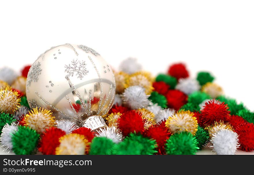 Silver Christmas bauble resting on colorful puff ball decoration over a white background. Silver Christmas bauble resting on colorful puff ball decoration over a white background