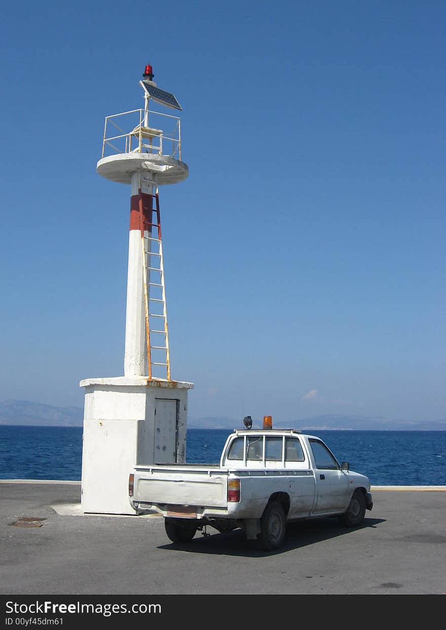 White lighthouse and a small car on the seaside in harbour of the island Kos in Greece