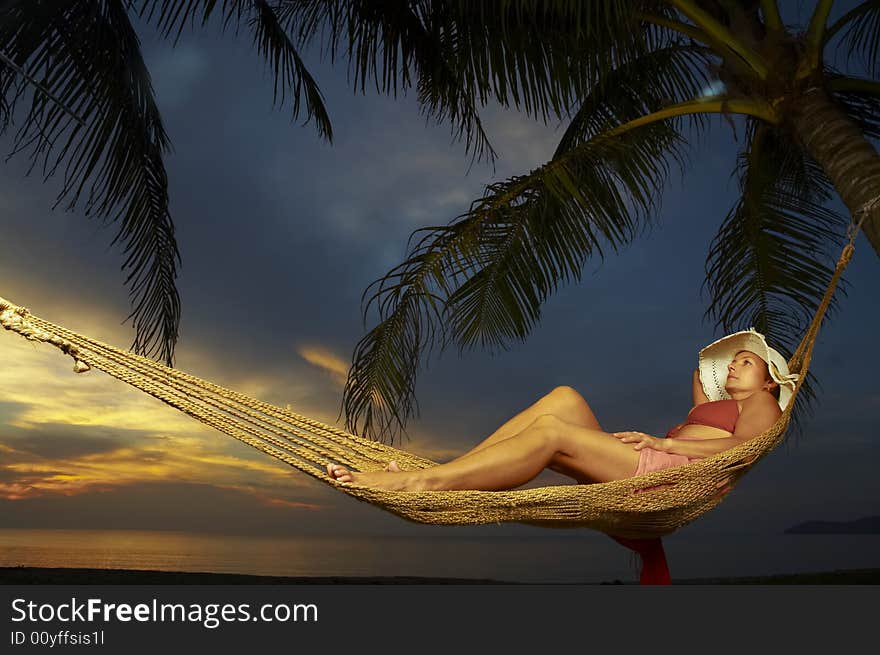 View of a woman lounging in hammock during sunset. View of a woman lounging in hammock during sunset