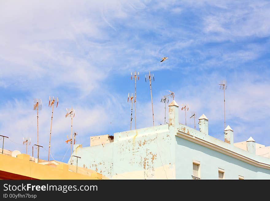 Antennas mounted on a roof and seagull in the blue sky. Antennas mounted on a roof and seagull in the blue sky