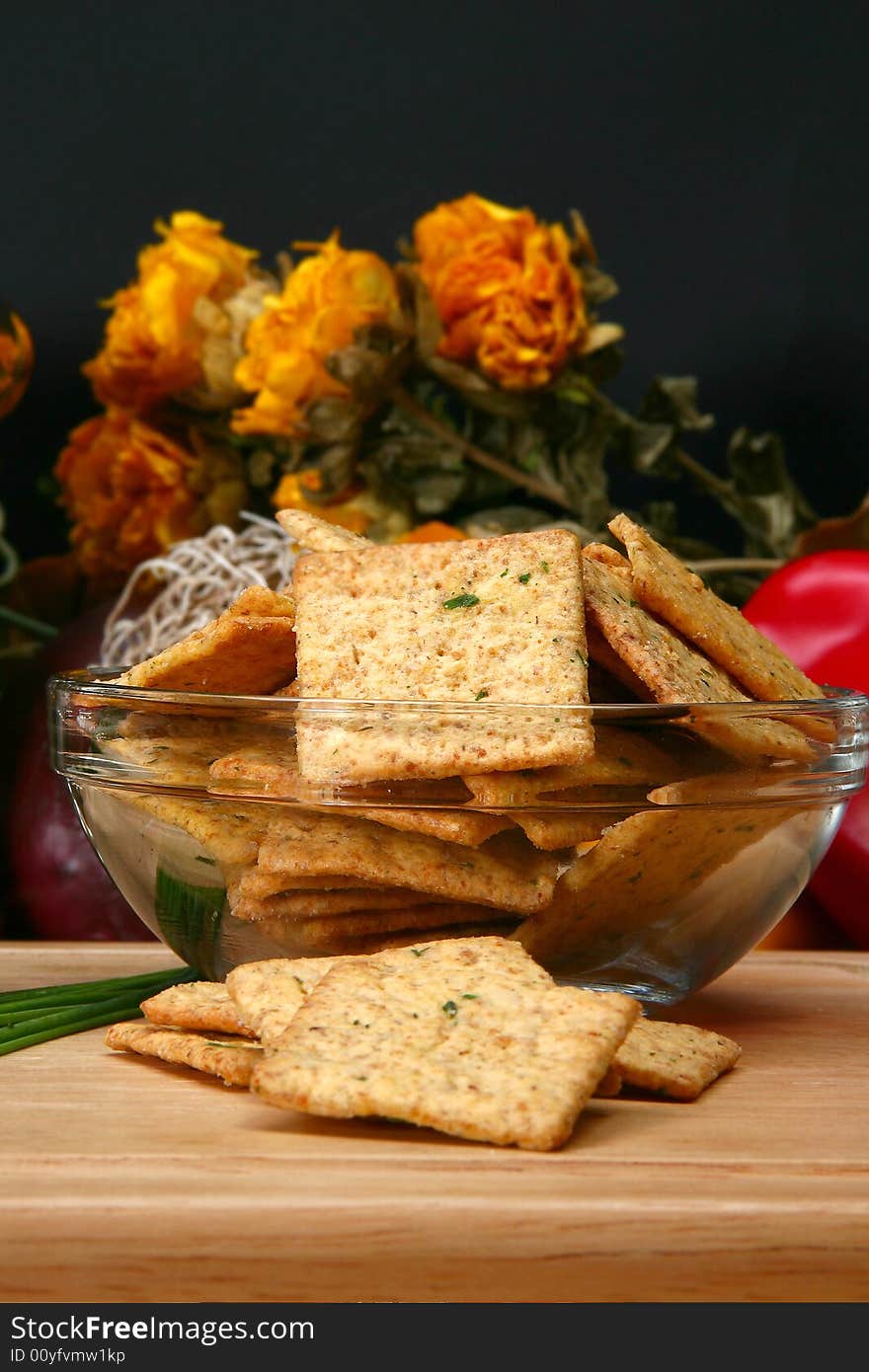 Square sour cream and chive flavored crackers in glass bowl on cutting board in kitchen or restaurant.