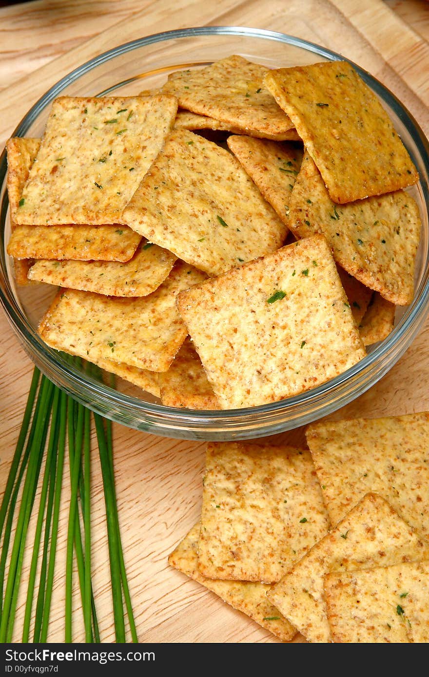 Square sour cream and chive flavored crackers in glass bowl on cutting board in kitchen or resturant.