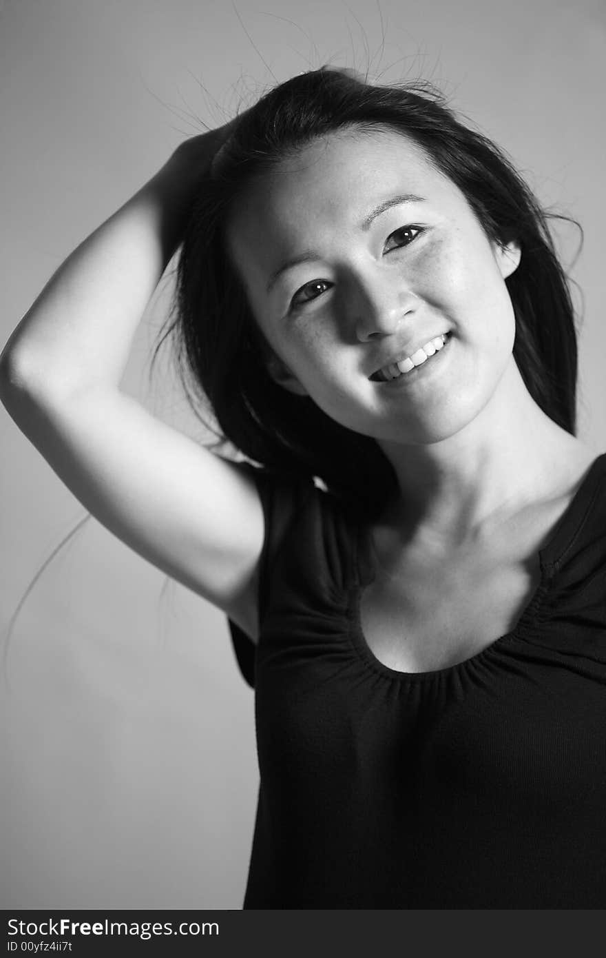 Black and white image of a young Asian woman with long hair pulling back from her smiling face. Black and white image of a young Asian woman with long hair pulling back from her smiling face.