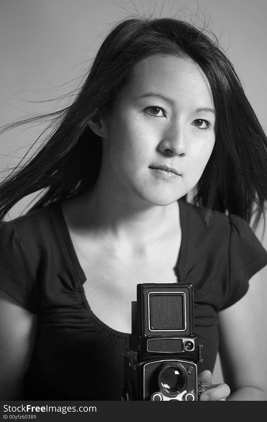 Black and white image of a young Asian woman taking a photograph with a medium format twin lens camera.