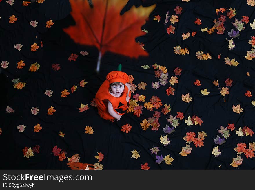 Pretty little girl dressed in a pumpkin costume, watching leaves fall from above; shot from above. Pretty little girl dressed in a pumpkin costume, watching leaves fall from above; shot from above.