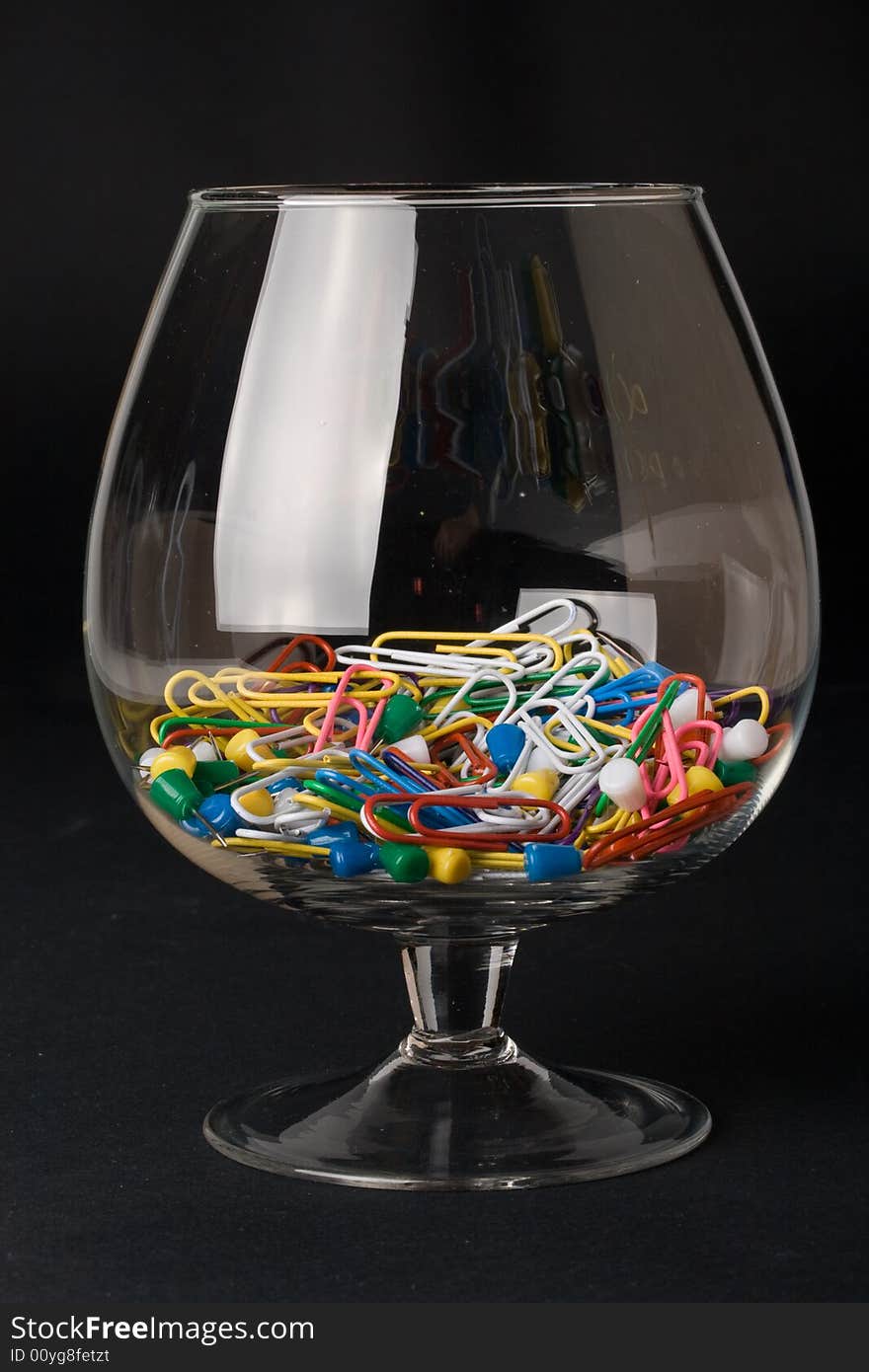 Colored paperclips and pins in a glass on a black background. Close up. Selective focus.