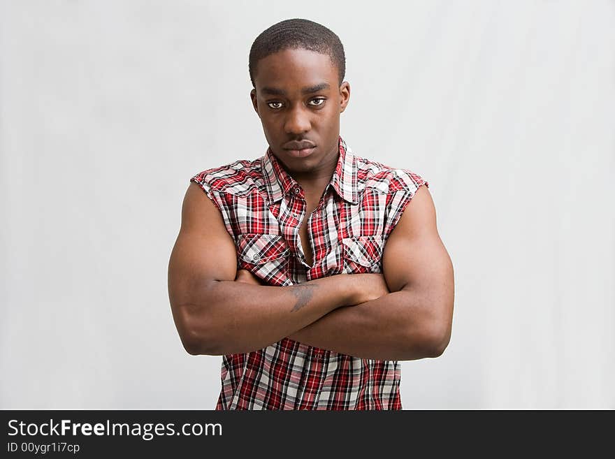 Young dark skinned handsome guy standing like a macho with both arms crossed wearing a checkerd shirt without sleeves. Young dark skinned handsome guy standing like a macho with both arms crossed wearing a checkerd shirt without sleeves.