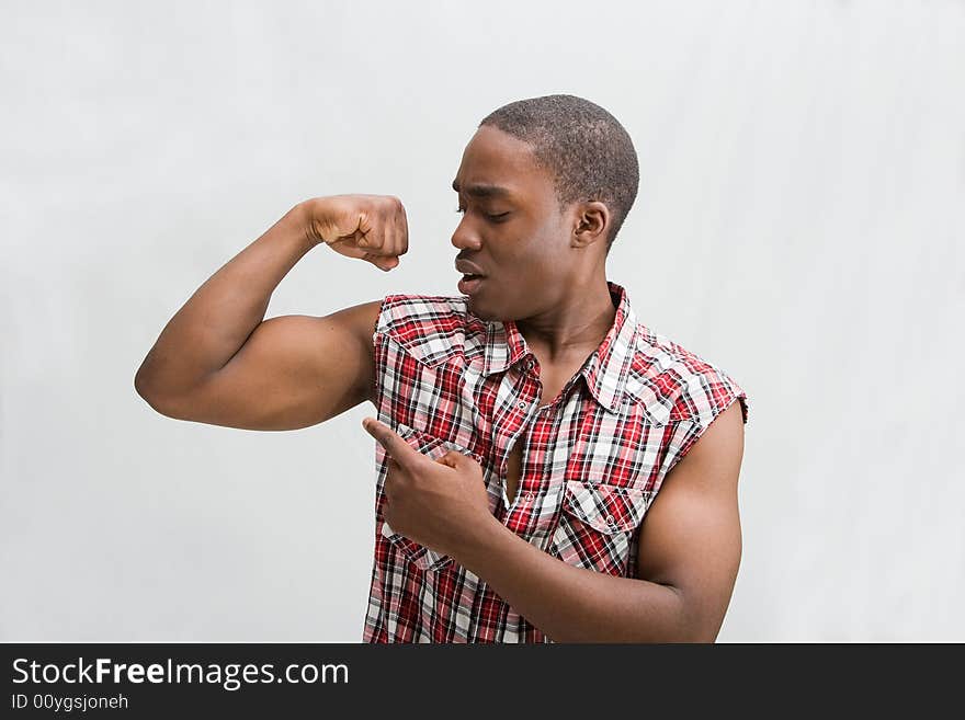 Young dark skinned handsome guy proudly pointing at his biceps showing how strong he is wearing a checkered shirt, isaolated. Young dark skinned handsome guy proudly pointing at his biceps showing how strong he is wearing a checkered shirt, isaolated