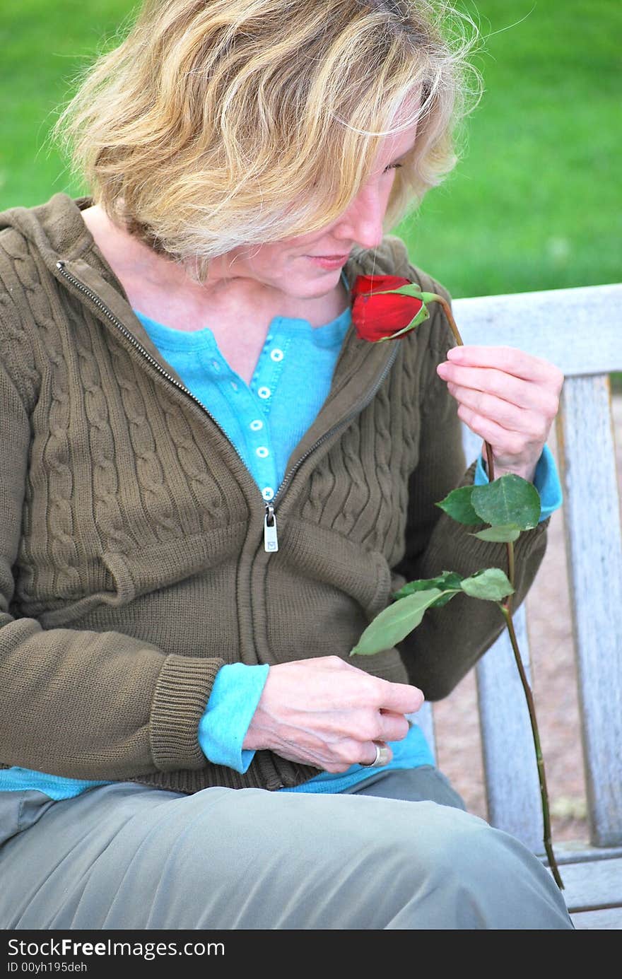 Woman smelling a rose left on her bench by her lover who is jogging around the park. Woman smelling a rose left on her bench by her lover who is jogging around the park.