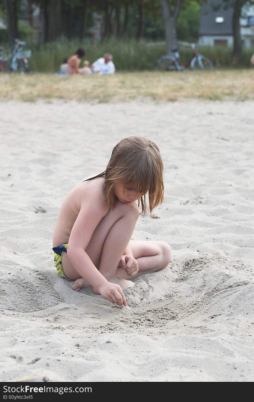 A little girl is drawing on a beach by a lake. A little girl is drawing on a beach by a lake.