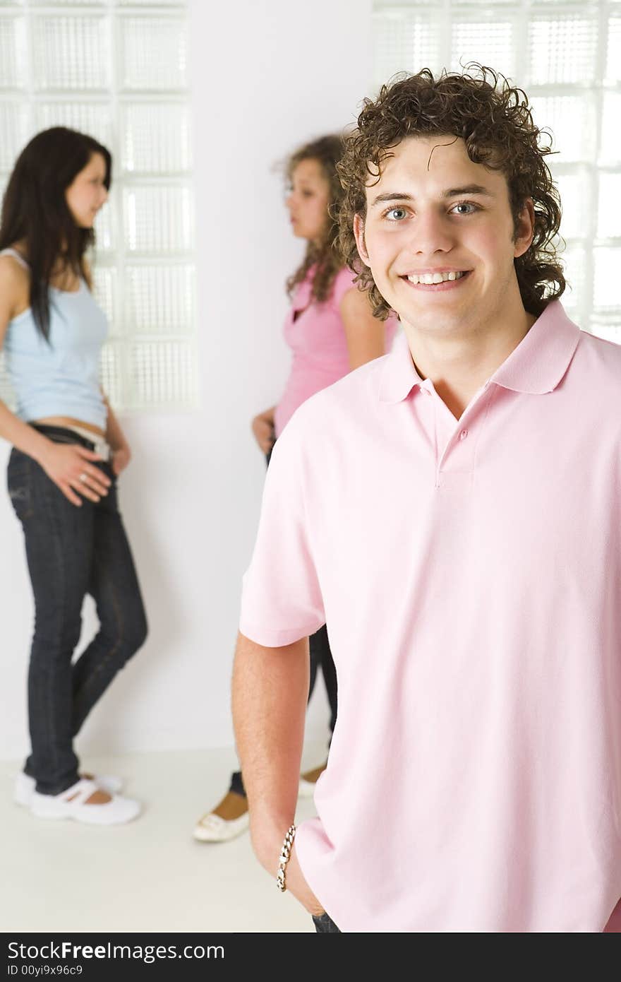 Three friends standing near window. A girls talking with themselves. A boy smiling and looking at camera. Focused on a boy. Three friends standing near window. A girls talking with themselves. A boy smiling and looking at camera. Focused on a boy.