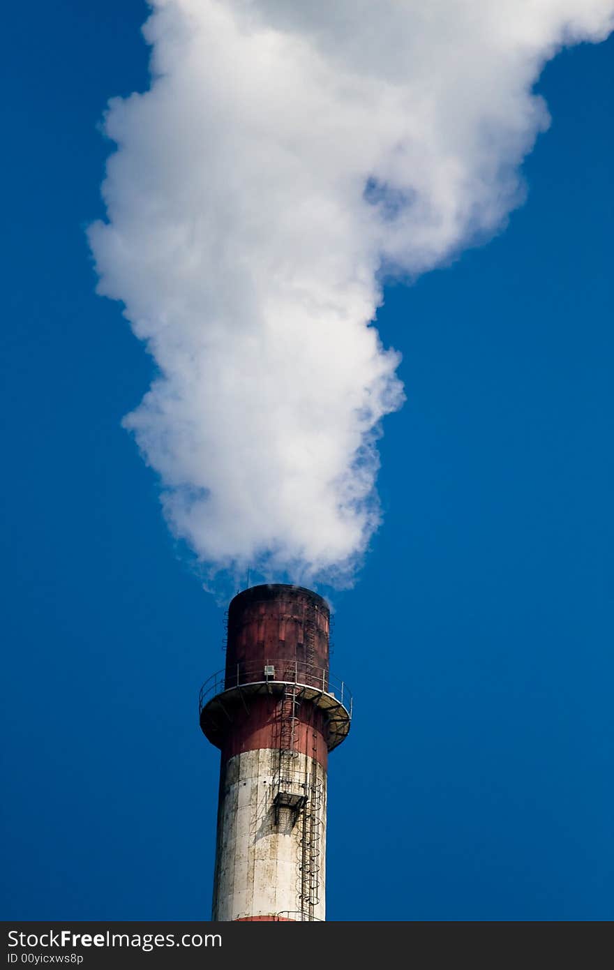 A cooling chimney pumping out white smoke against a blue sky background. A cooling chimney pumping out white smoke against a blue sky background