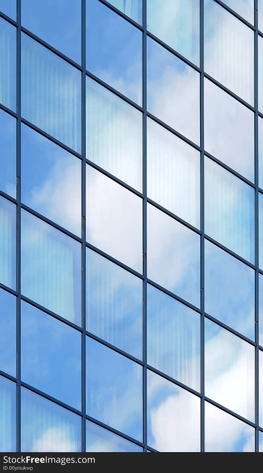 Modern, glass facade of office building. Cloud and sky reflexions plus some glass transparency show a bit interiors with curtains.