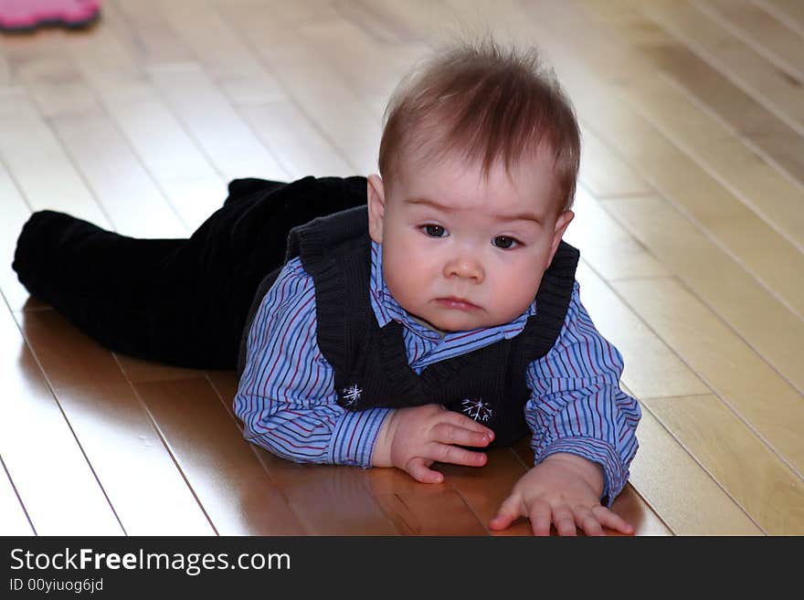 A baby boy dressed in a shirt and vest for the holidays crawling on the hardwood floor. A baby boy dressed in a shirt and vest for the holidays crawling on the hardwood floor