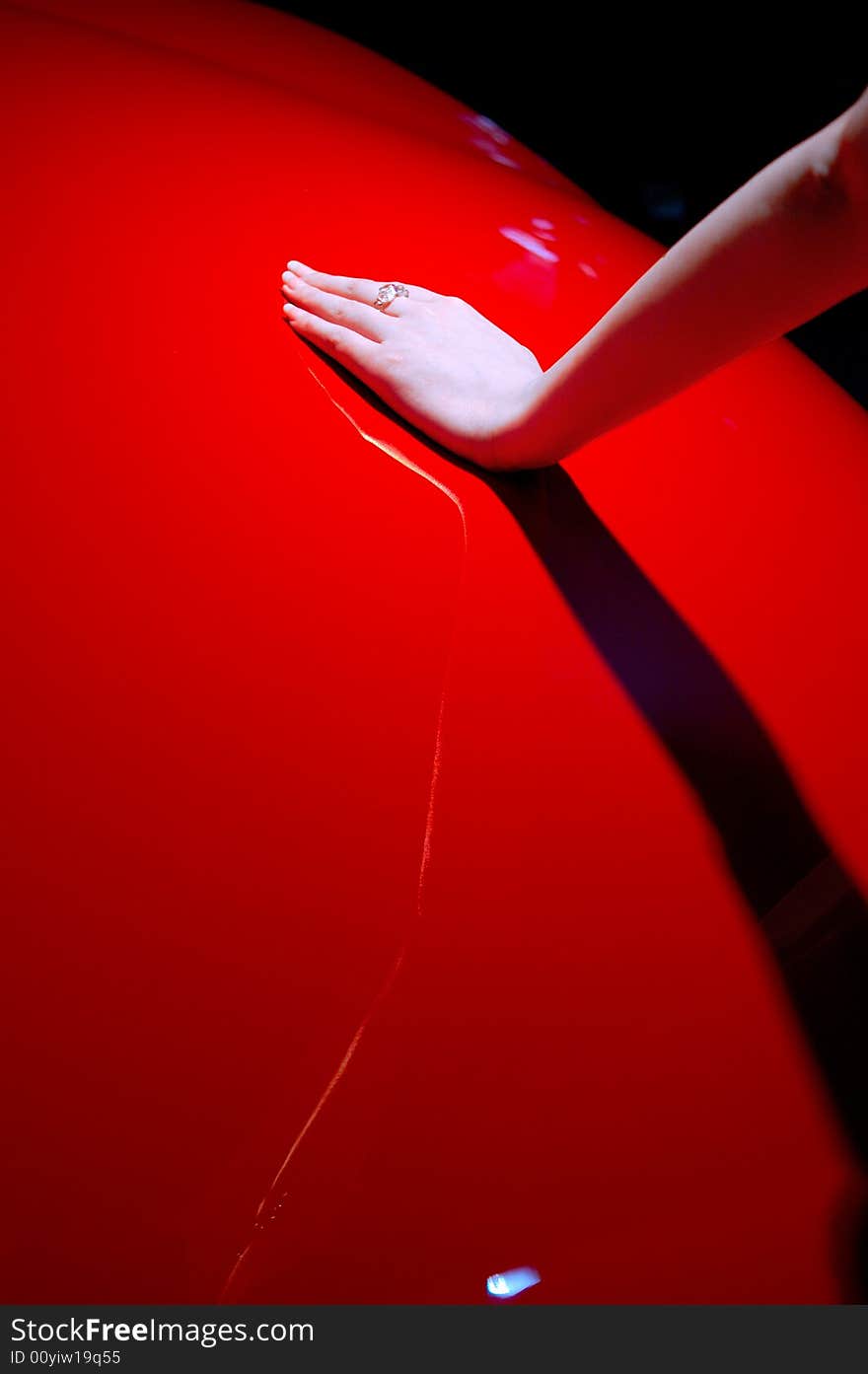 A hand of a young chinese lady supports on a red car. there is a ring wearing on her finger.  Hand and its' shadow are forming an X character. A hand of a young chinese lady supports on a red car. there is a ring wearing on her finger.  Hand and its' shadow are forming an X character.