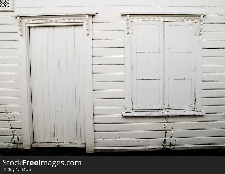 Wall of an white house with painted window and missing door handle. Wall of an white house with painted window and missing door handle.