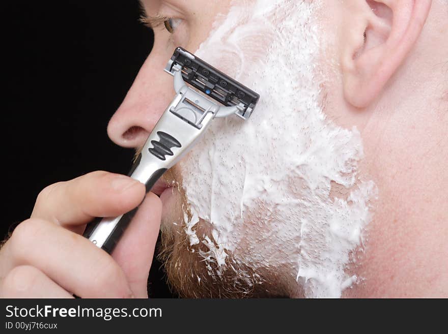 A young man shaves the side of his face to clean up his goatee. A young man shaves the side of his face to clean up his goatee.