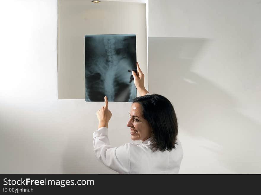 Female Doctor points at an x-ray of a person's spine while she smiles and laughs. Horizontally framed photograph. Female Doctor points at an x-ray of a person's spine while she smiles and laughs. Horizontally framed photograph