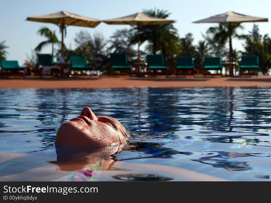 A young woman is relaxing in the pool. Ideal vacation shot with sun umbrellas and palm trees in the back. A young woman is relaxing in the pool. Ideal vacation shot with sun umbrellas and palm trees in the back.