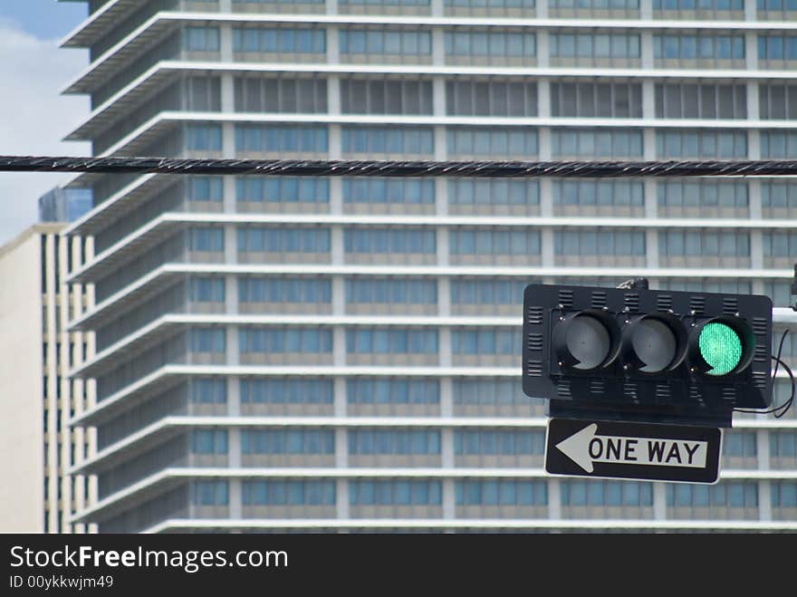 A traffic light on green with one way sign below and out of focus buildig in background. A traffic light on green with one way sign below and out of focus buildig in background.