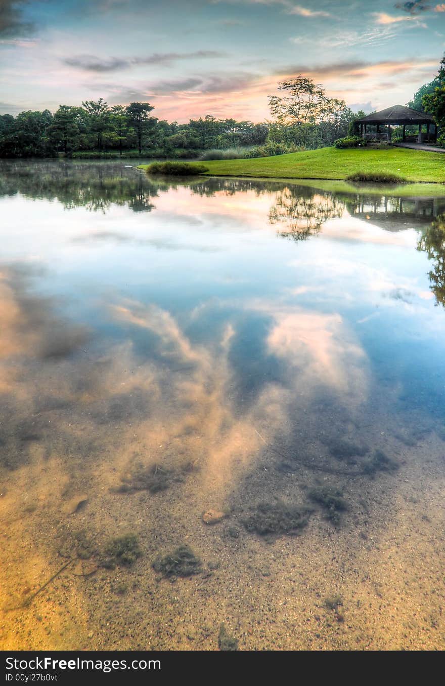 Fiery red clouds reflected in a the still clear shallow lake with a pavilion on the far bank. Fiery red clouds reflected in a the still clear shallow lake with a pavilion on the far bank