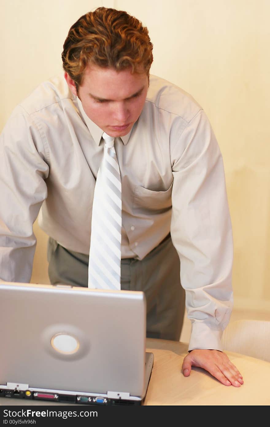 Front view of businessman in tan shirt standing over open laptop computer. Front view of businessman in tan shirt standing over open laptop computer