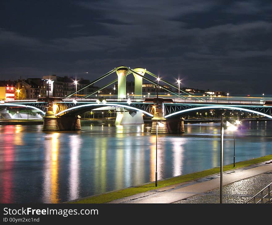 A bridge over a river lit up at nigh by a number of lights. A bridge over a river lit up at nigh by a number of lights