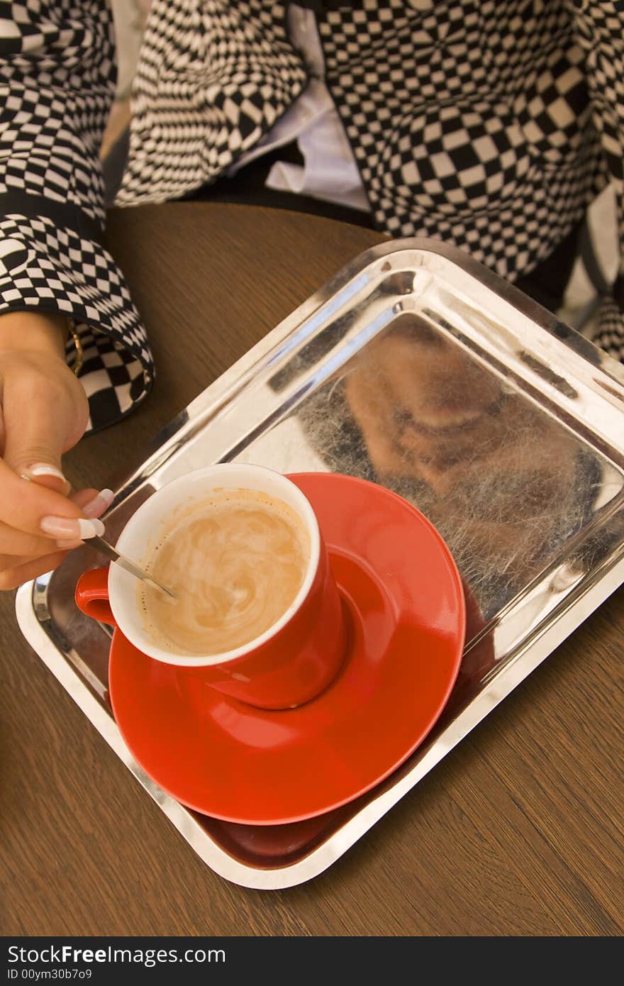 Detail view of a woman's hand mixing the sugar in a coffee cup. Detail view of a woman's hand mixing the sugar in a coffee cup.