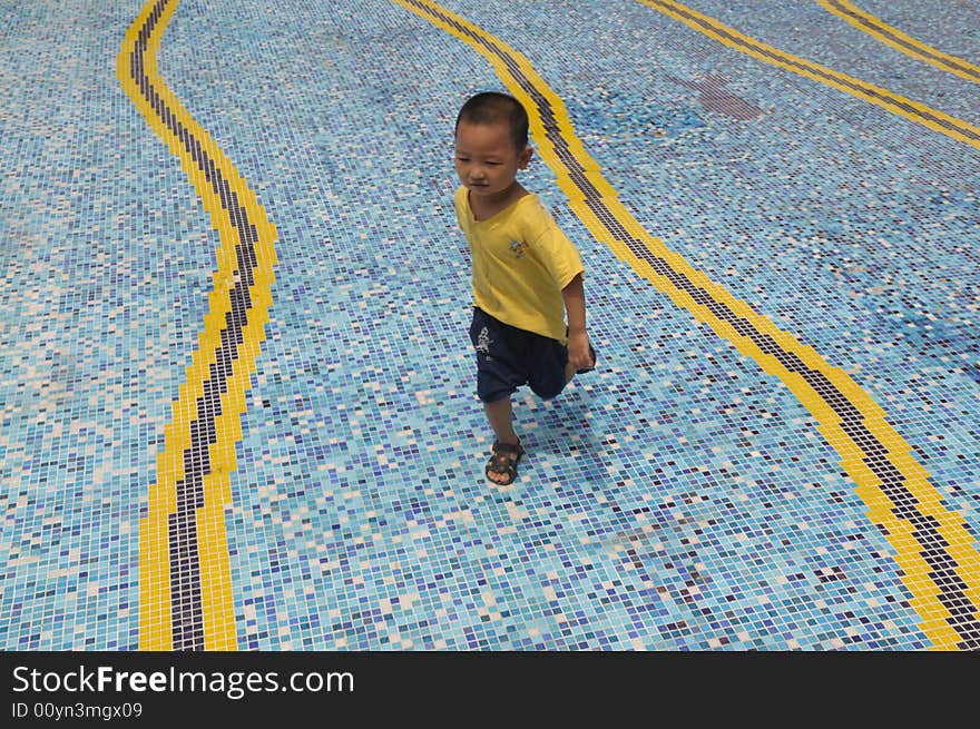 A little Chinese boy running happily on the mosaic ground of a swimming pool. A little Chinese boy running happily on the mosaic ground of a swimming pool.