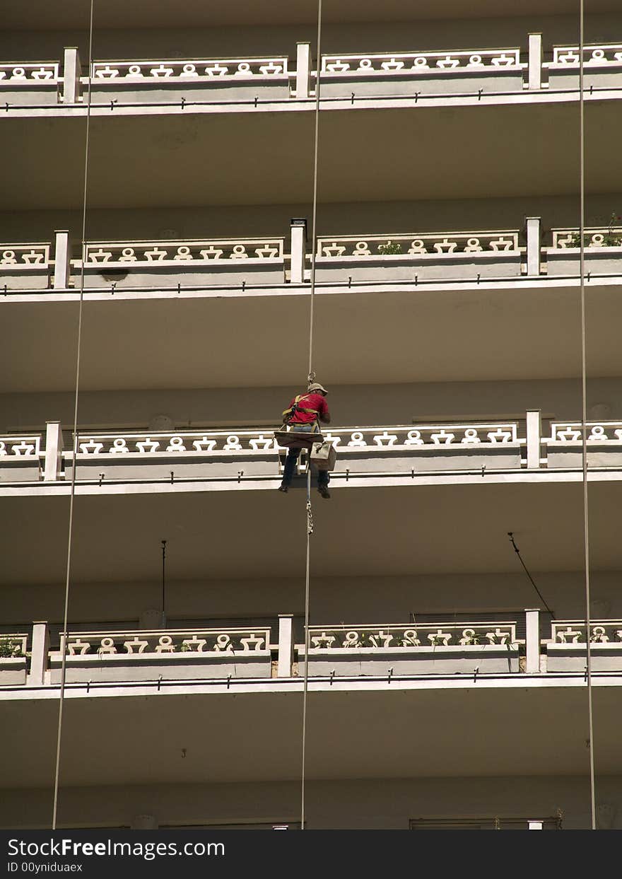 Man hanging at a facade of a house with balconies is cleaning the railings. Man hanging at a facade of a house with balconies is cleaning the railings