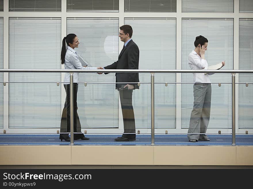 Businessman and businesswoman shaking hands on modern office corridor. three persons. Businessman and businesswoman shaking hands on modern office corridor. three persons