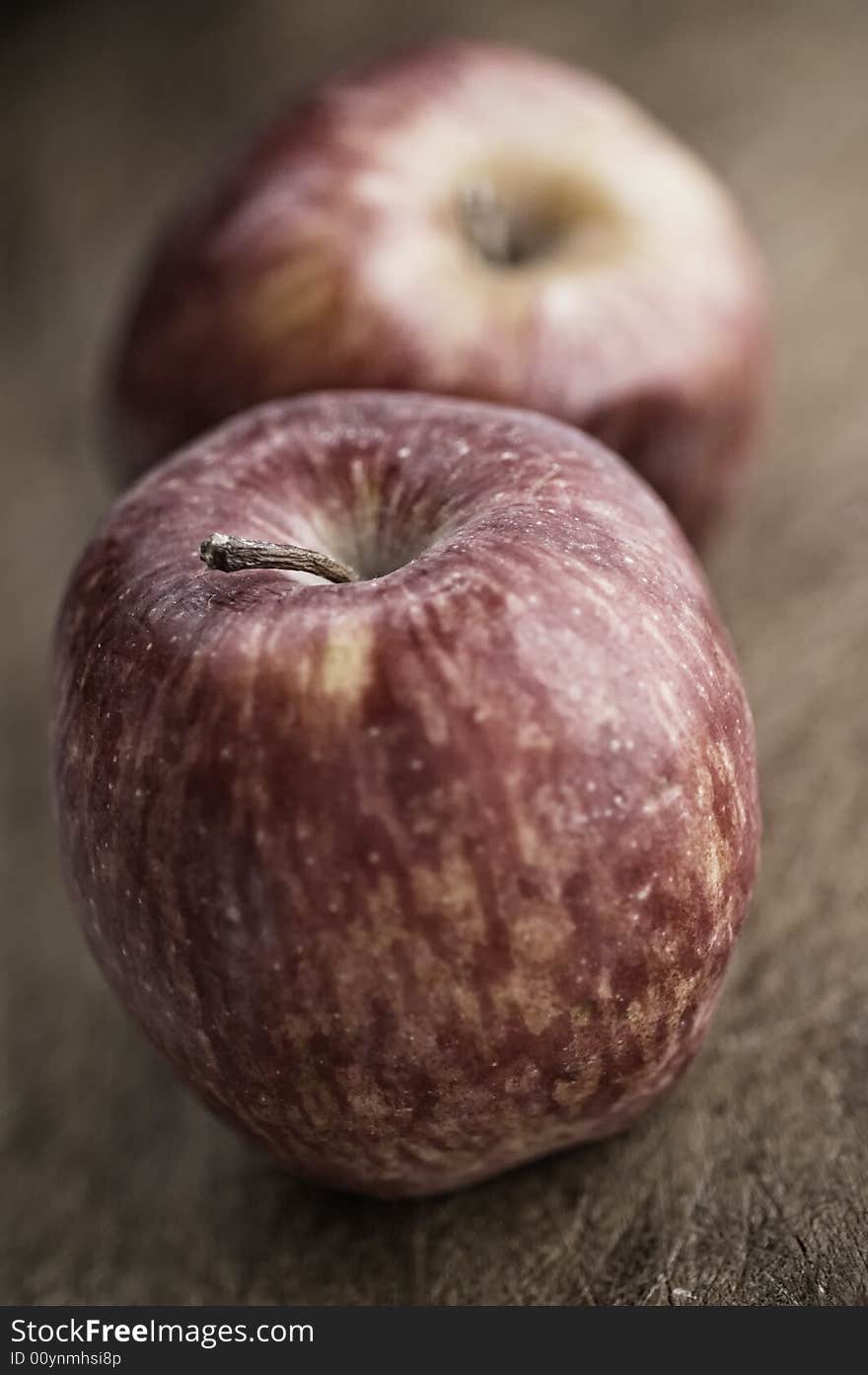 Two red apples on an old wooden kitchen table.