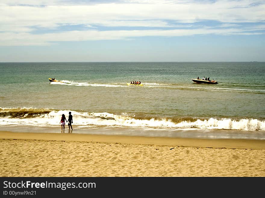 Sailing boats at sea and a couple walking along the beach at Puerto Vallarta, Mexico