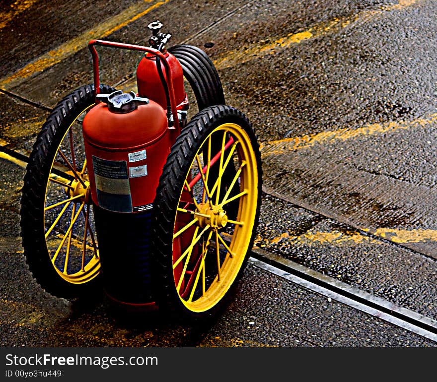 Fire Extinguisher on Wheels parked on the pavement with yellow lines. The photo has an antiquated essance look and feel to it.