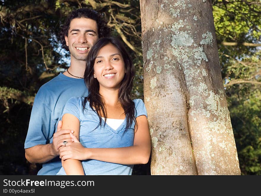 A Happy couple embraces in front of a tree. Horizontally framed photograph. A Happy couple embraces in front of a tree. Horizontally framed photograph.