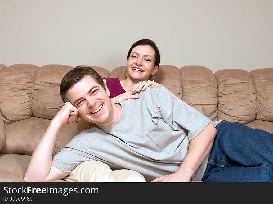 Smiling, happy couple sitting on a couch. They are laughing as he lays across her lap. Horizontally framed photograph. Smiling, happy couple sitting on a couch. They are laughing as he lays across her lap. Horizontally framed photograph